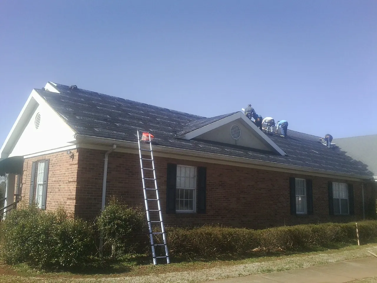 Crew tearing shingles off a brick ranch roof with a ladder set — Emergency Roof Repair work by our crew in Brooks