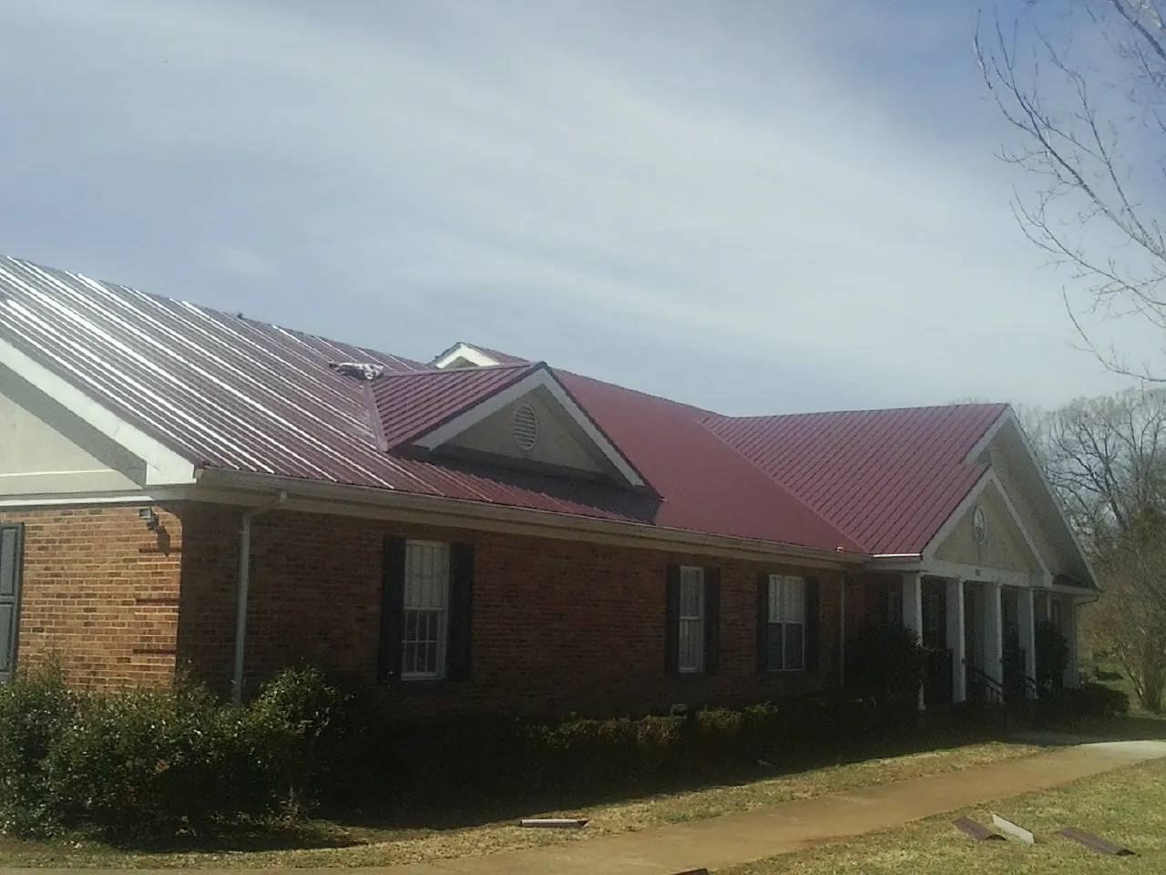 Red metal roof with gabled entries on a long brick building, from a Hail Damage Roof Repair job in Brooks
