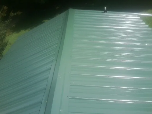 New green metal panels meeting at the ridge of a roof — Flat Roof Repair work by our crew in Brooks