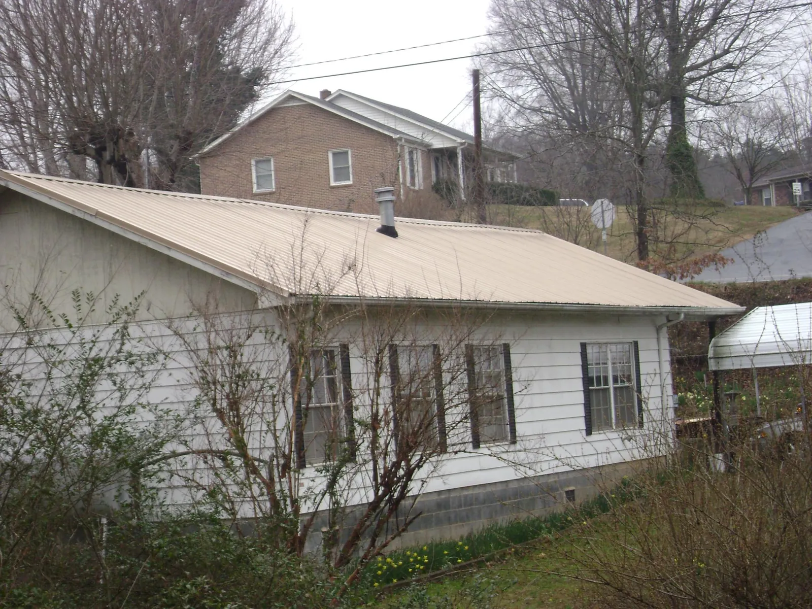 Tan metal roof on a white sided house set into a hillside — Commercial Roofing by Roofing Brothers in Brooks