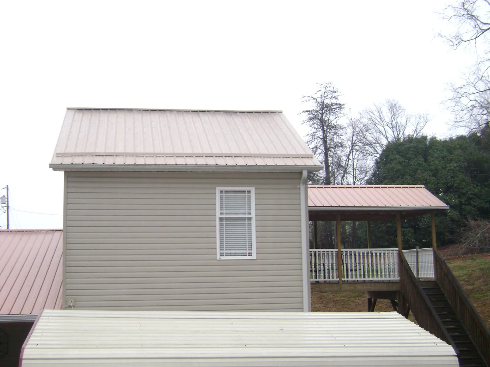 Tan metal roofs on a two story addition and attached porch, from a Roof Replacement job in Brooks